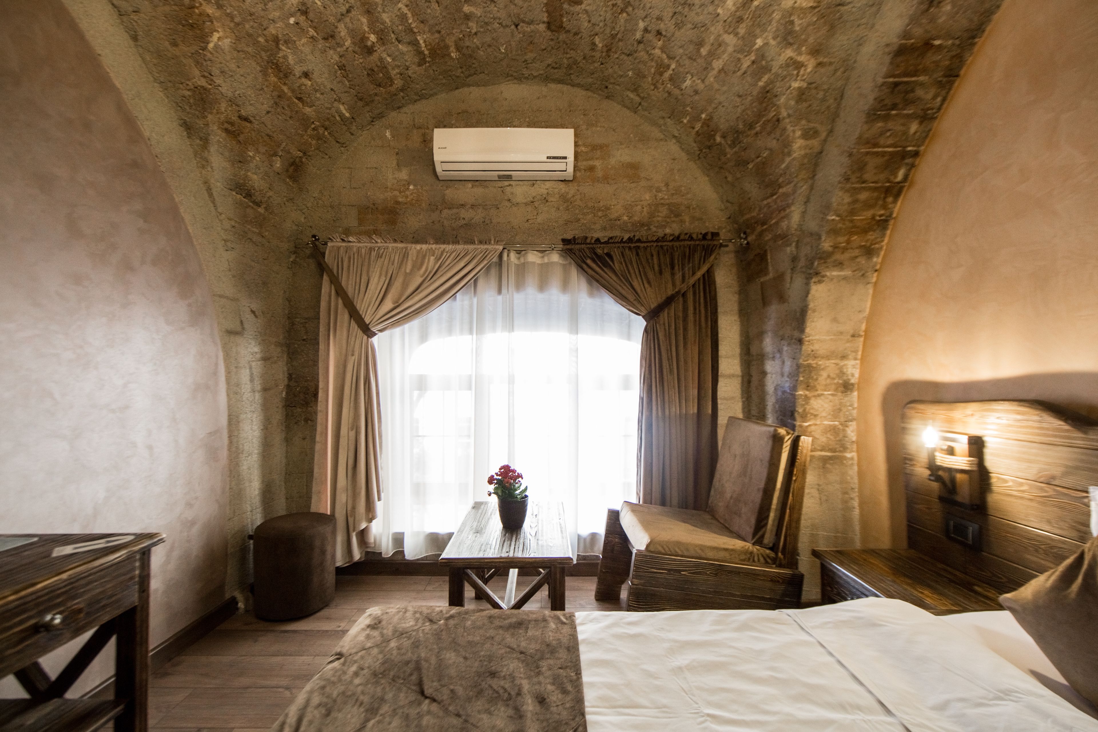 A room with a bed, a wooden table with a vase, a sofa, and a wall-mounted air conditioner.