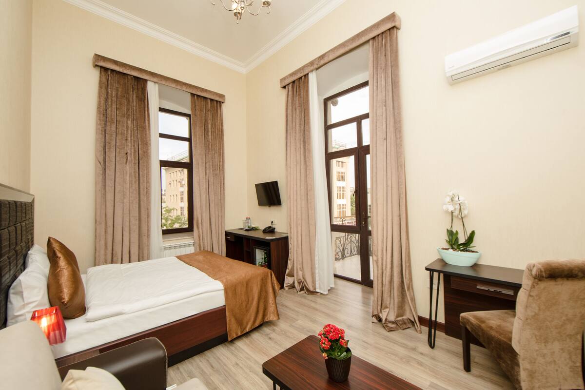 Ein Hotelzimmer mit Bett, Schreibtisch, Stuhl, Fernseher und einem Fenster mit Vorhängen.