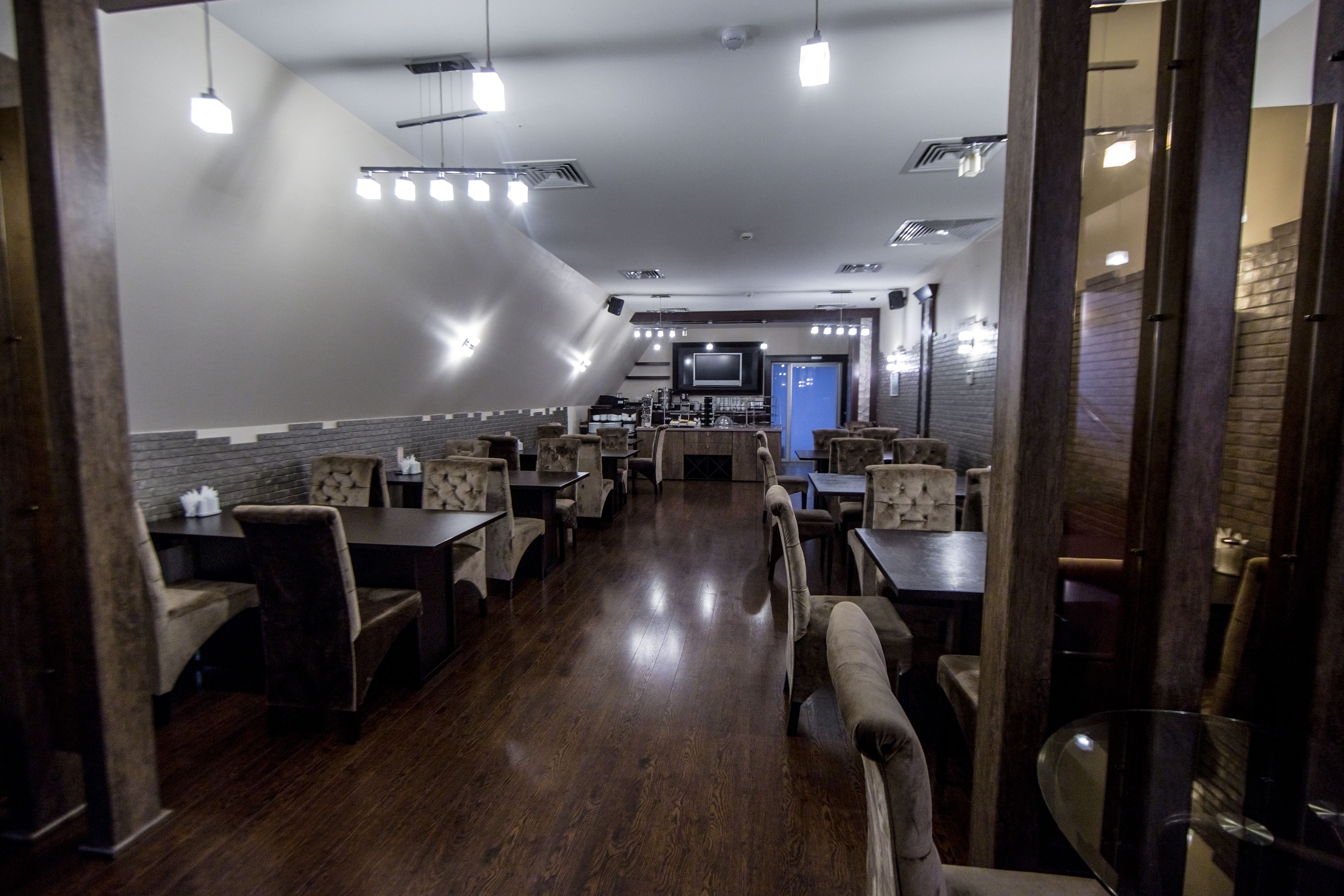 Un restaurant amb sòl de fusta, diverses taules i caires, i una televisió al fons.