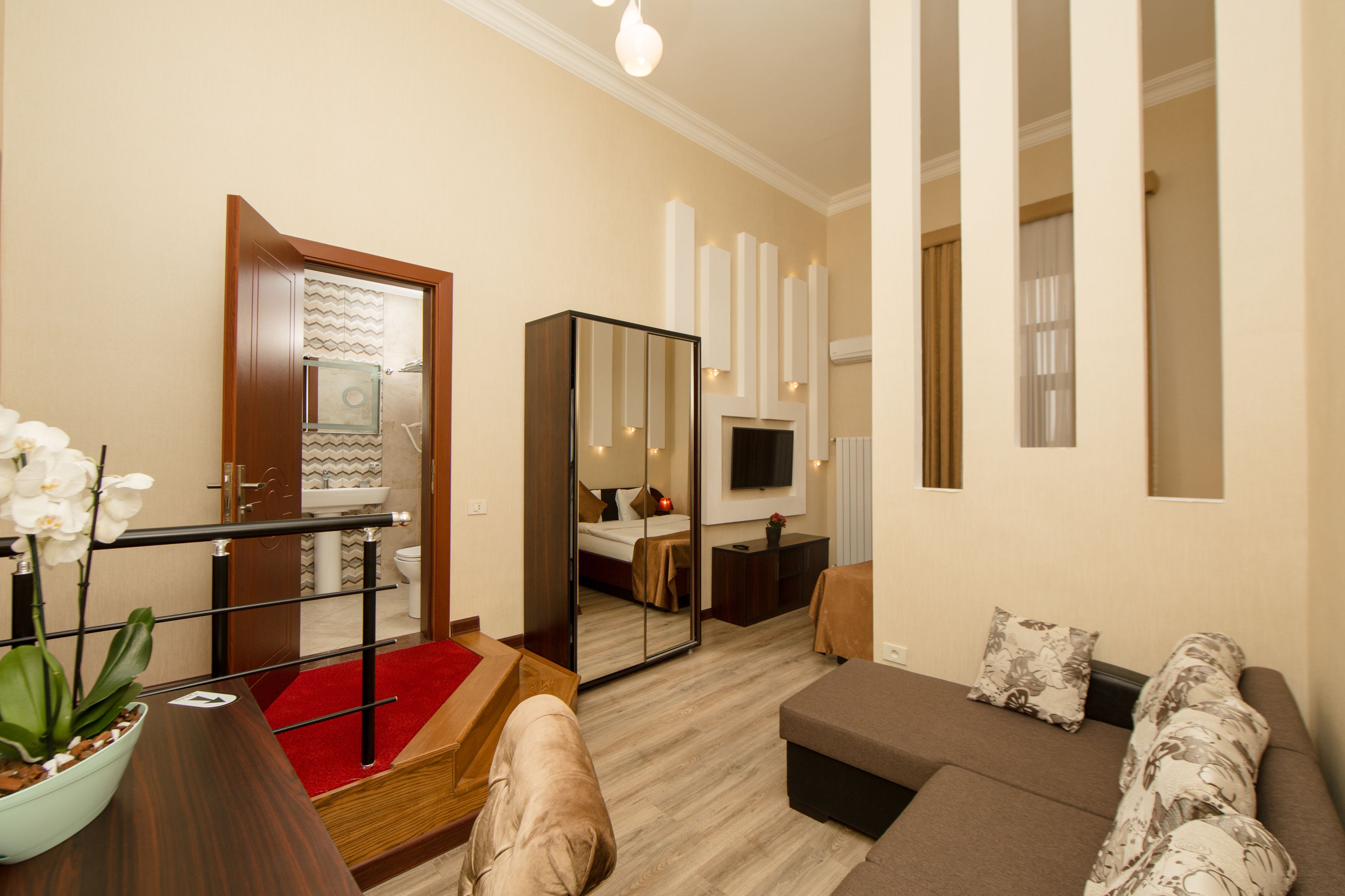 Una habitación de hotel moderna con sofá, una mesita, un espejo, televisión y alfombra roja.