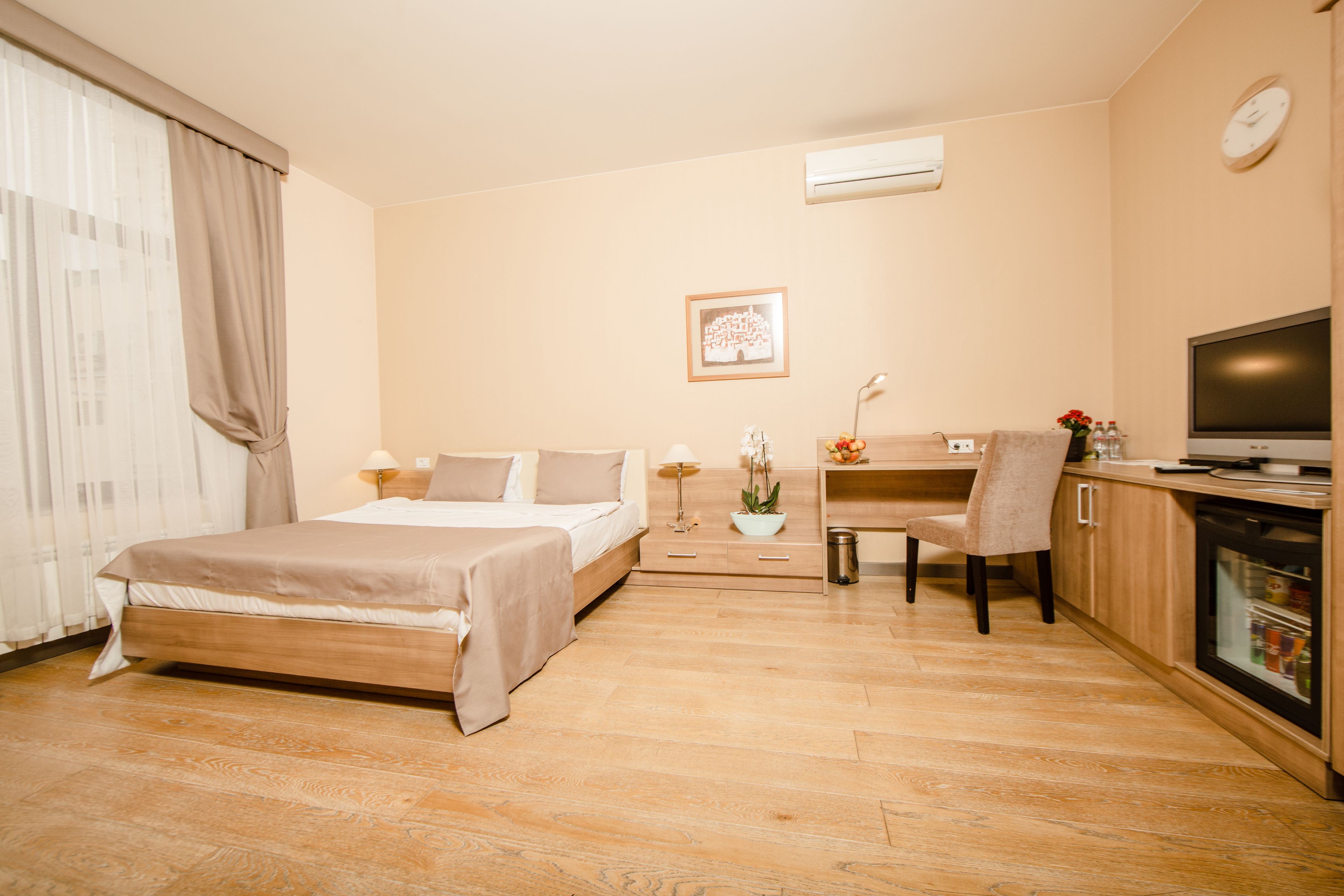 A hotel room with a bed, a desk with a computer, a chair, a TV, and a small table with a plant.