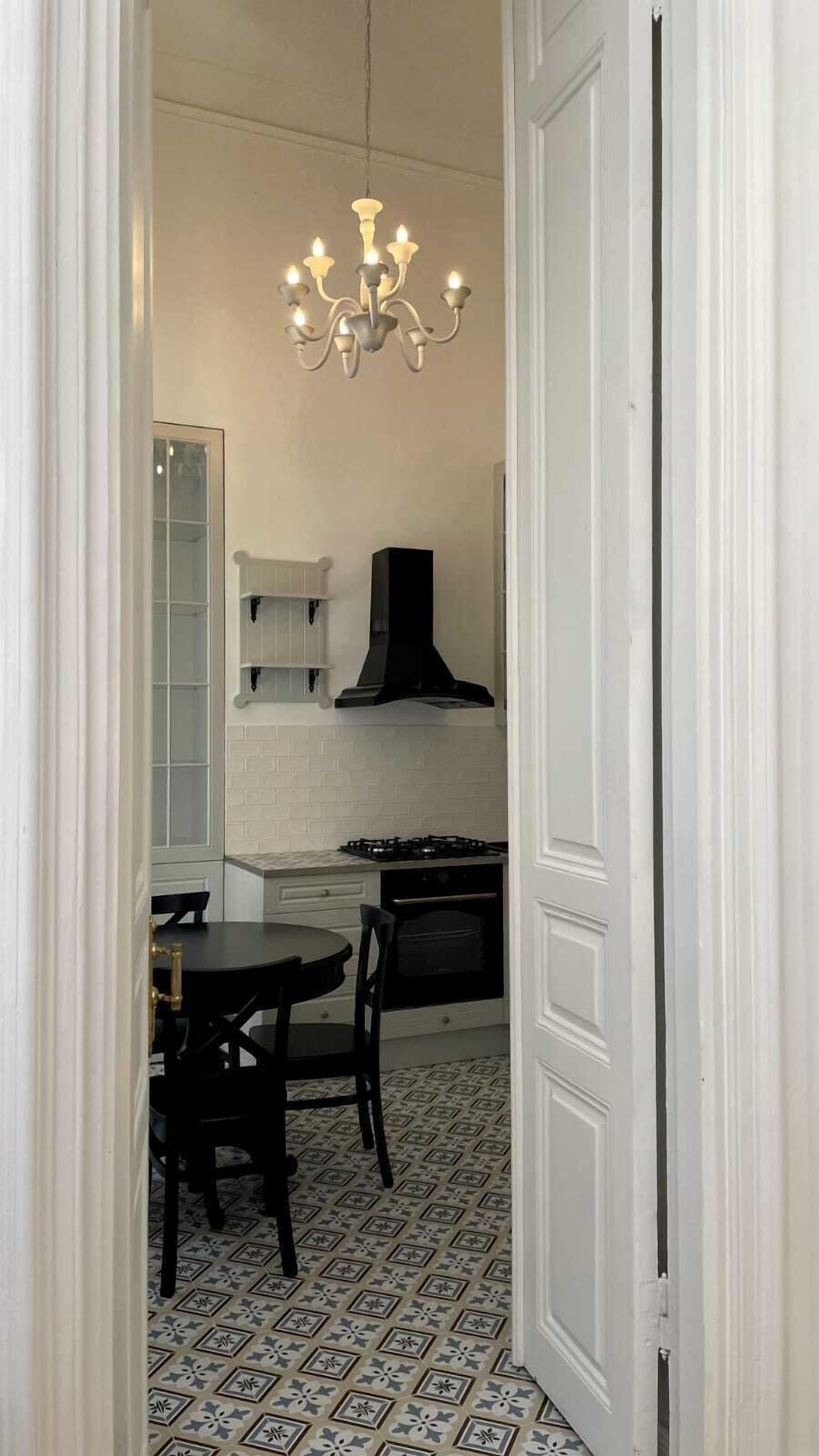 A compact kitchen with a gas stove, a black range hood, and a chandelier.