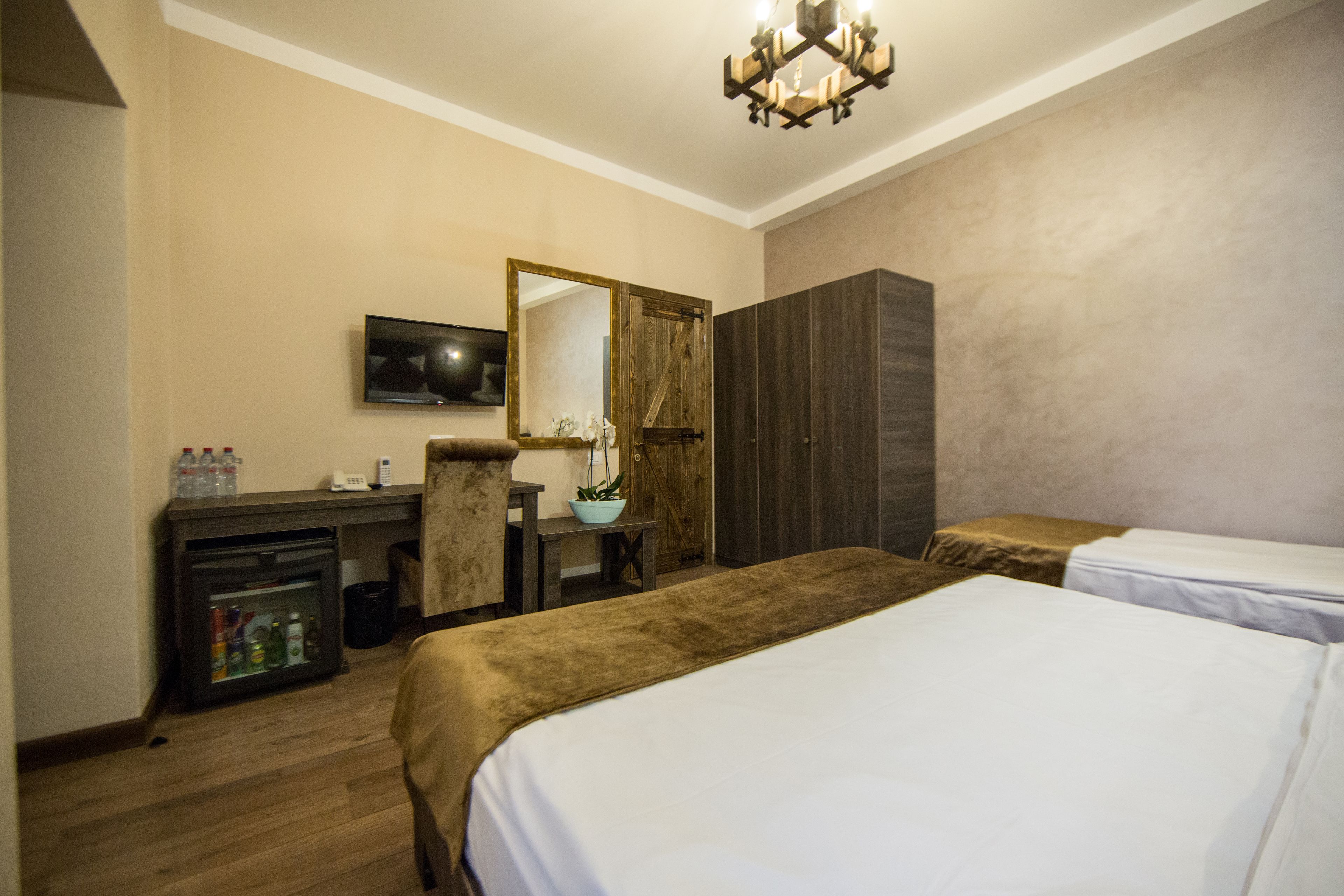 A hotel room with a bed, a desk with a mirror, a television, and a minibar.