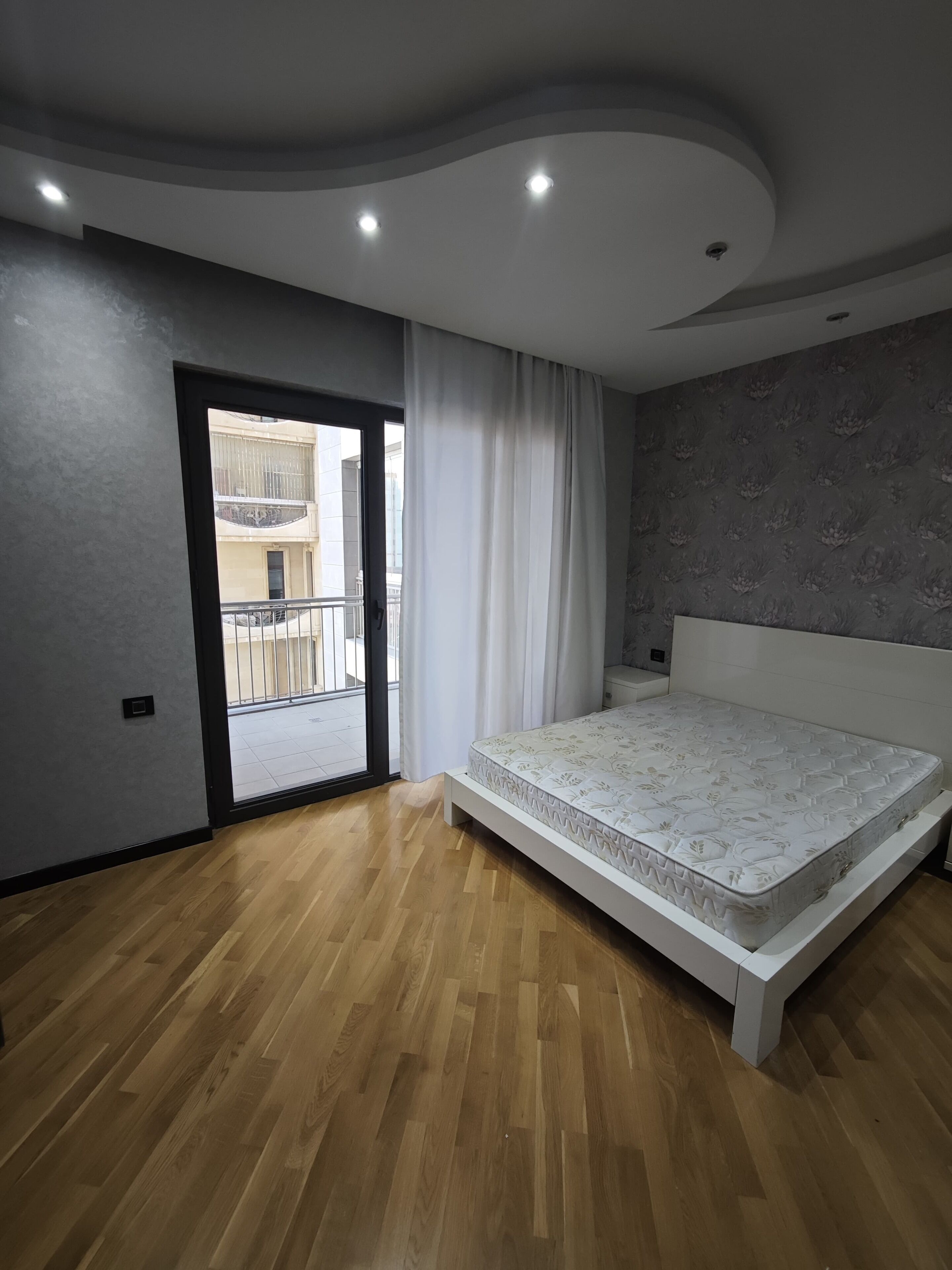 A modern bedroom with a large bed, a balcony, and a view of a building.