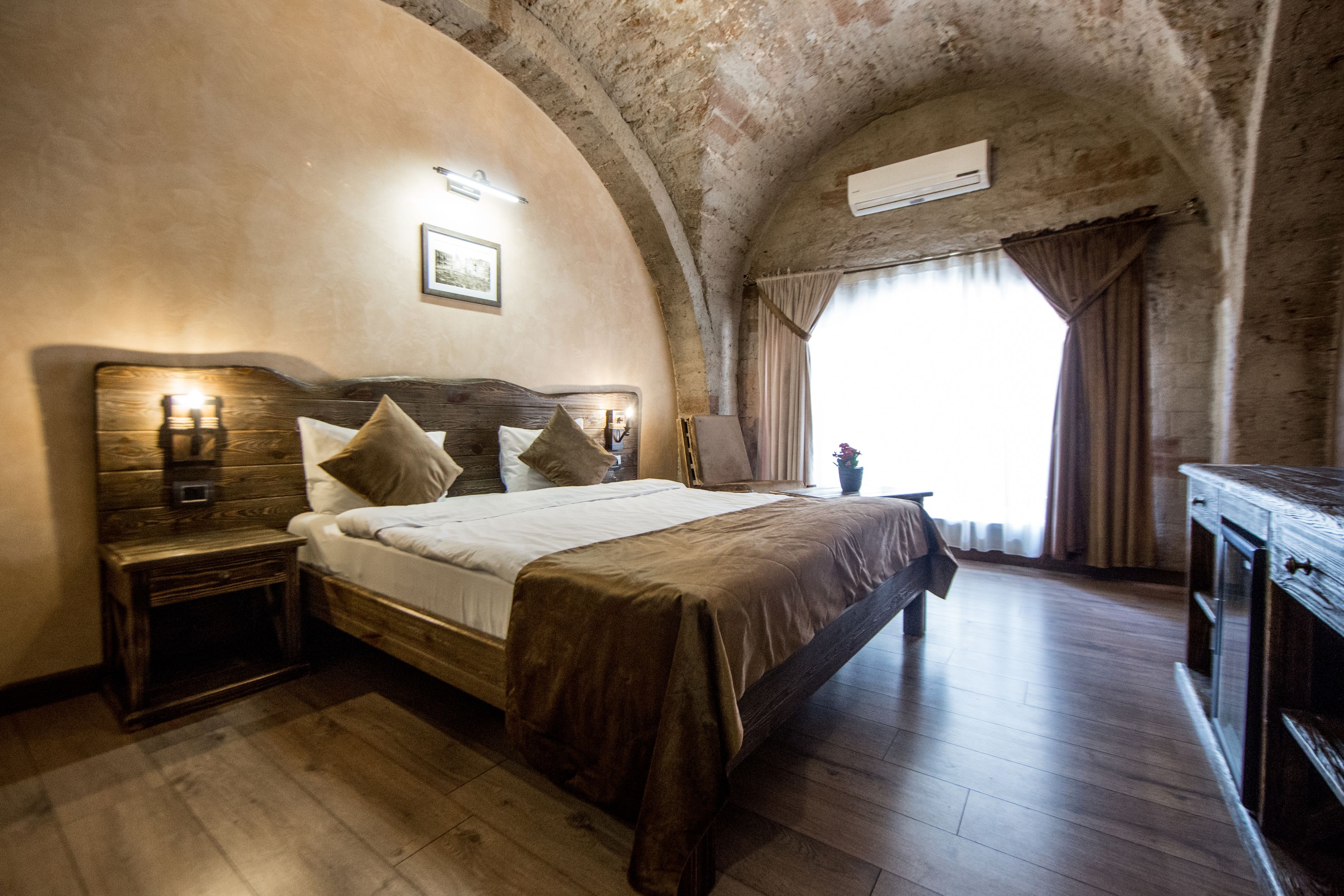 A bedroom with a large bed, wooden headboard, bedside tables, a dresser, and a window with curtains.