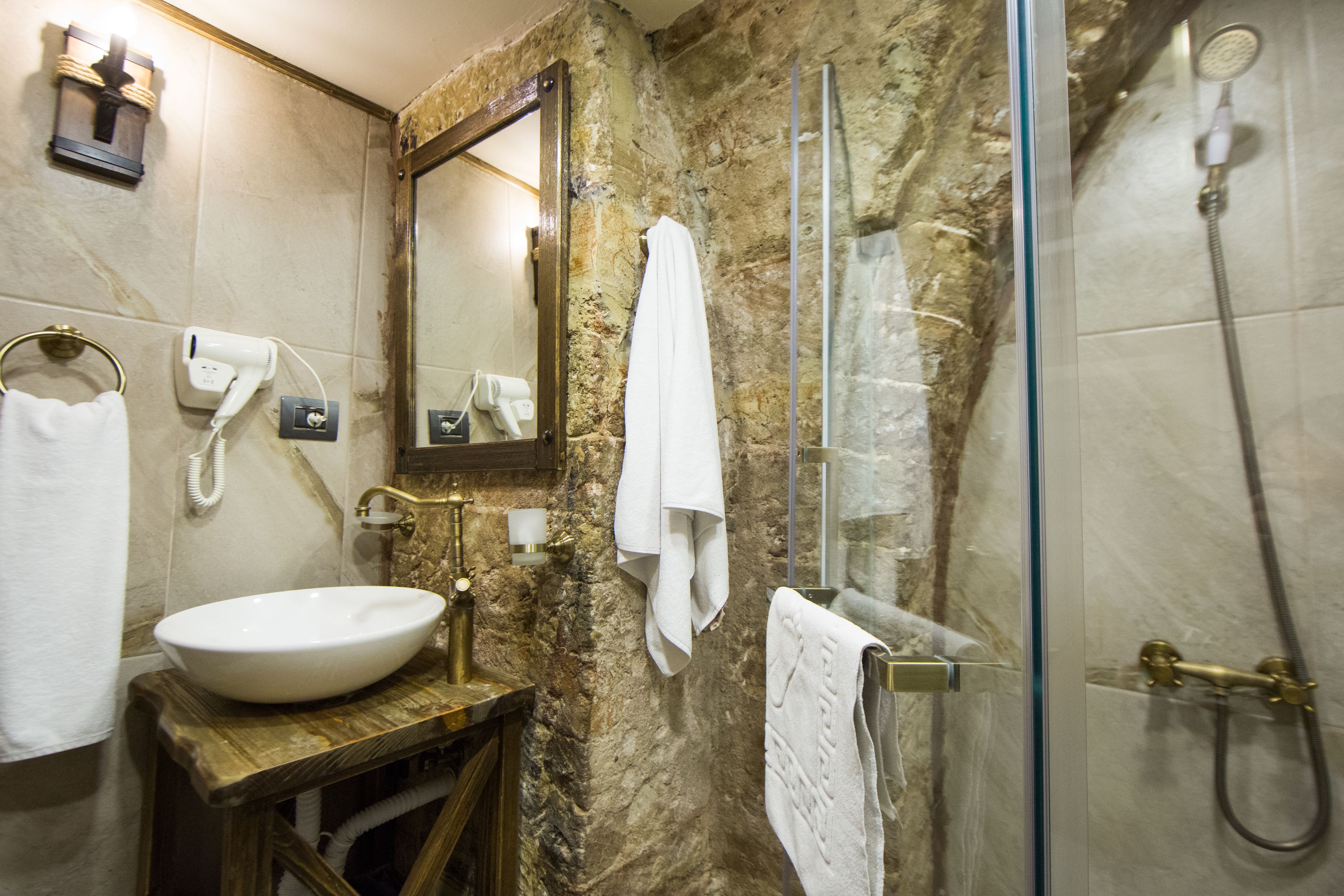A bathroom with a marble wall, a wooden vanity, a white sink, a mirror, a towel rack, and a glass-enclosed shower.