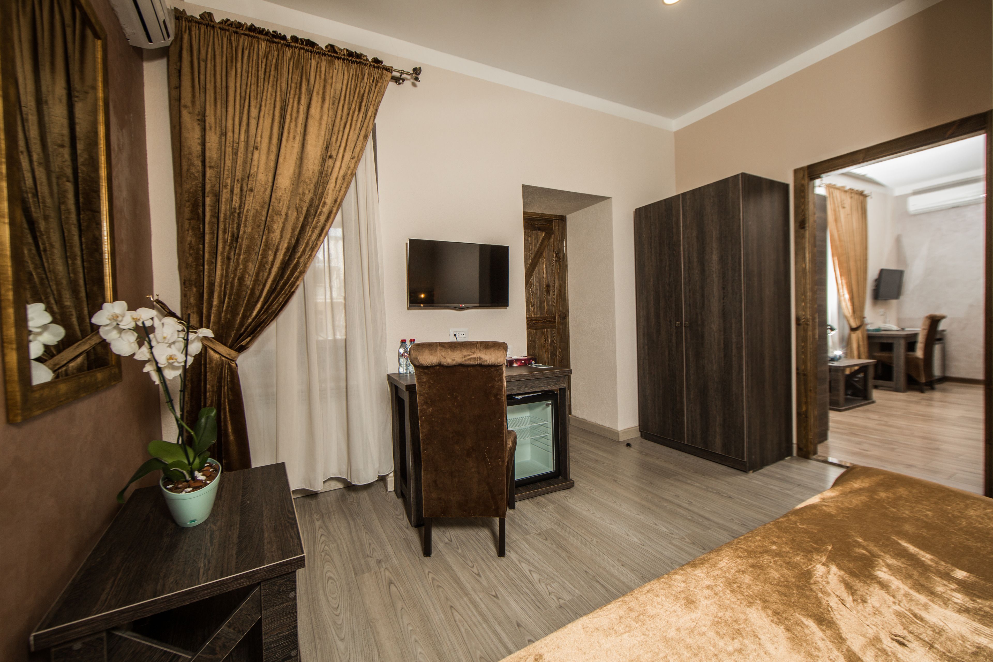 Una habitación de hotel con un escritorio de madera, un televisor montado en la pared, un refrigerador pequeño y una cama grande.