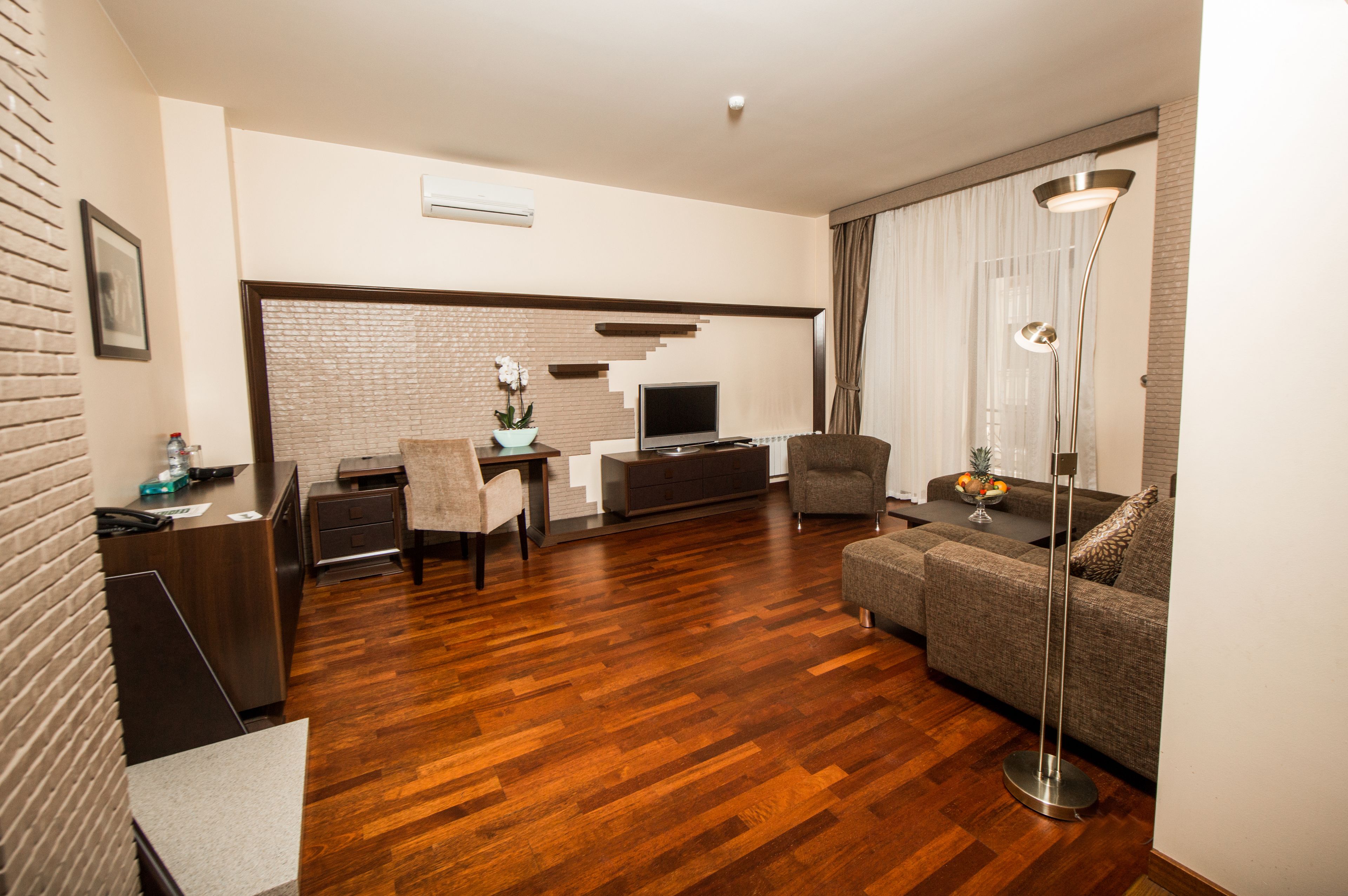 A modern living room with hardwood flooring, a grey sofa, a coffee table, a TV, and a desk with a chair.