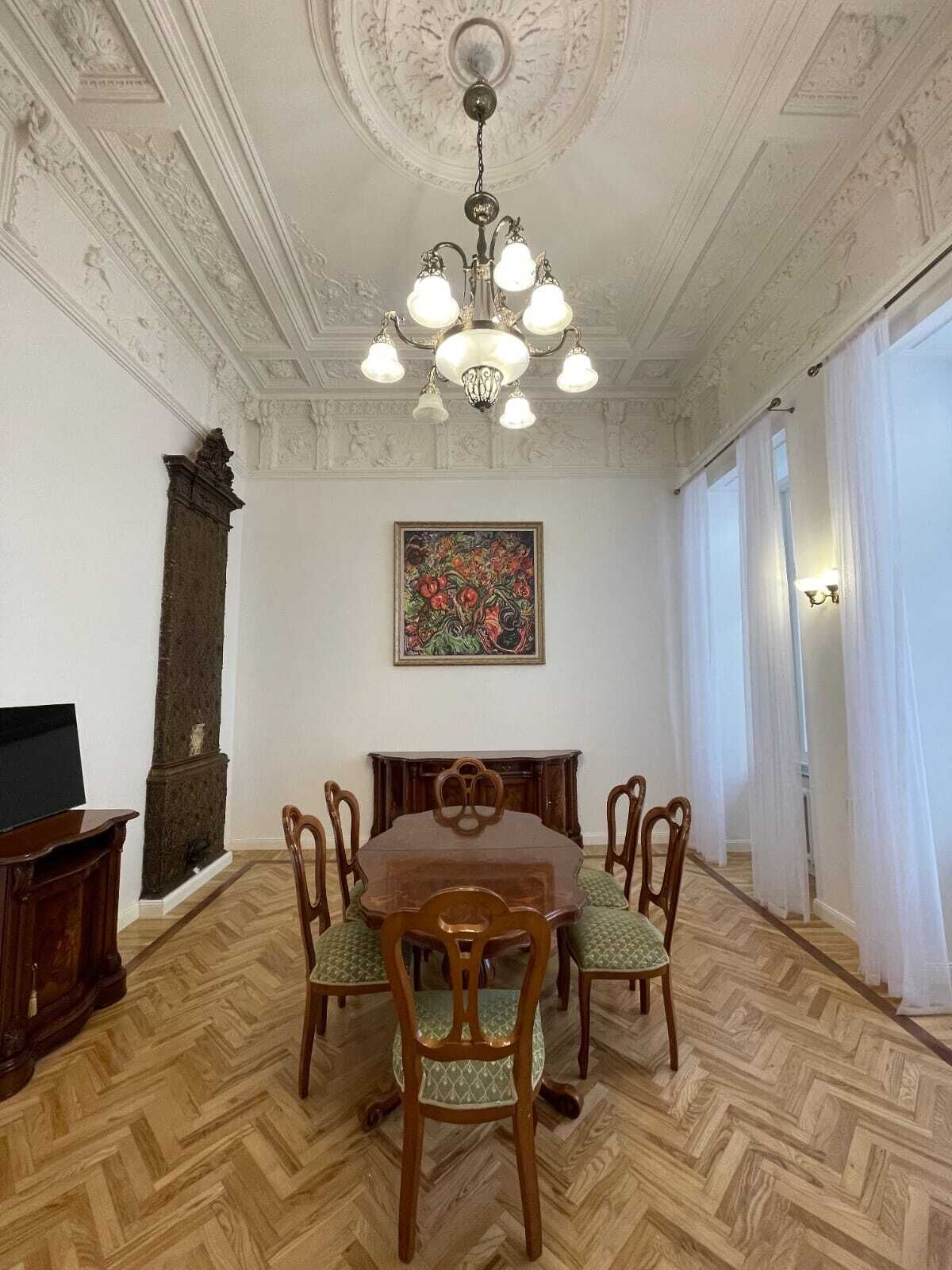 Une salle à manger avec une table en bois, six chaises, un lustre, une cheminée et un tableau au mur.
