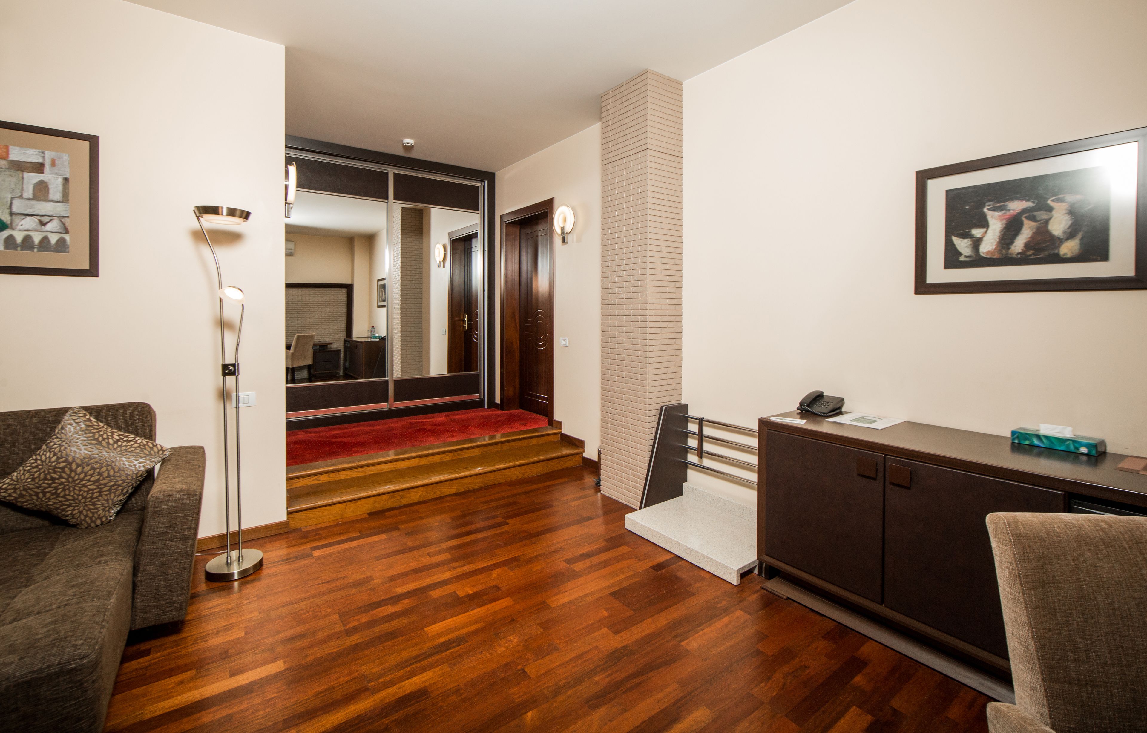 Une chambre d’hôtel avec un plancher en bois, un canapé, un bureau avec un téléphone et un miroir.