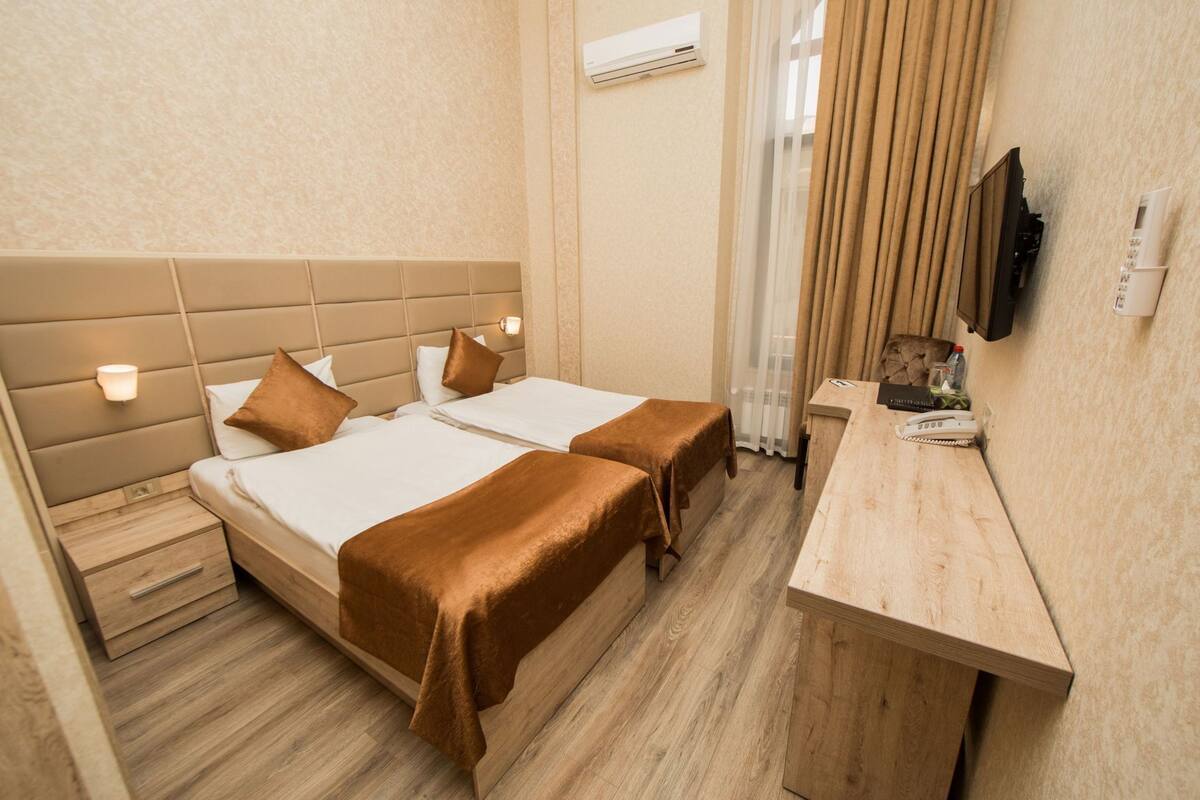 Ein Hotelzimmer mit zwei Betten, einem Holztisch, einem Fernseher und einer Klimaanlage.