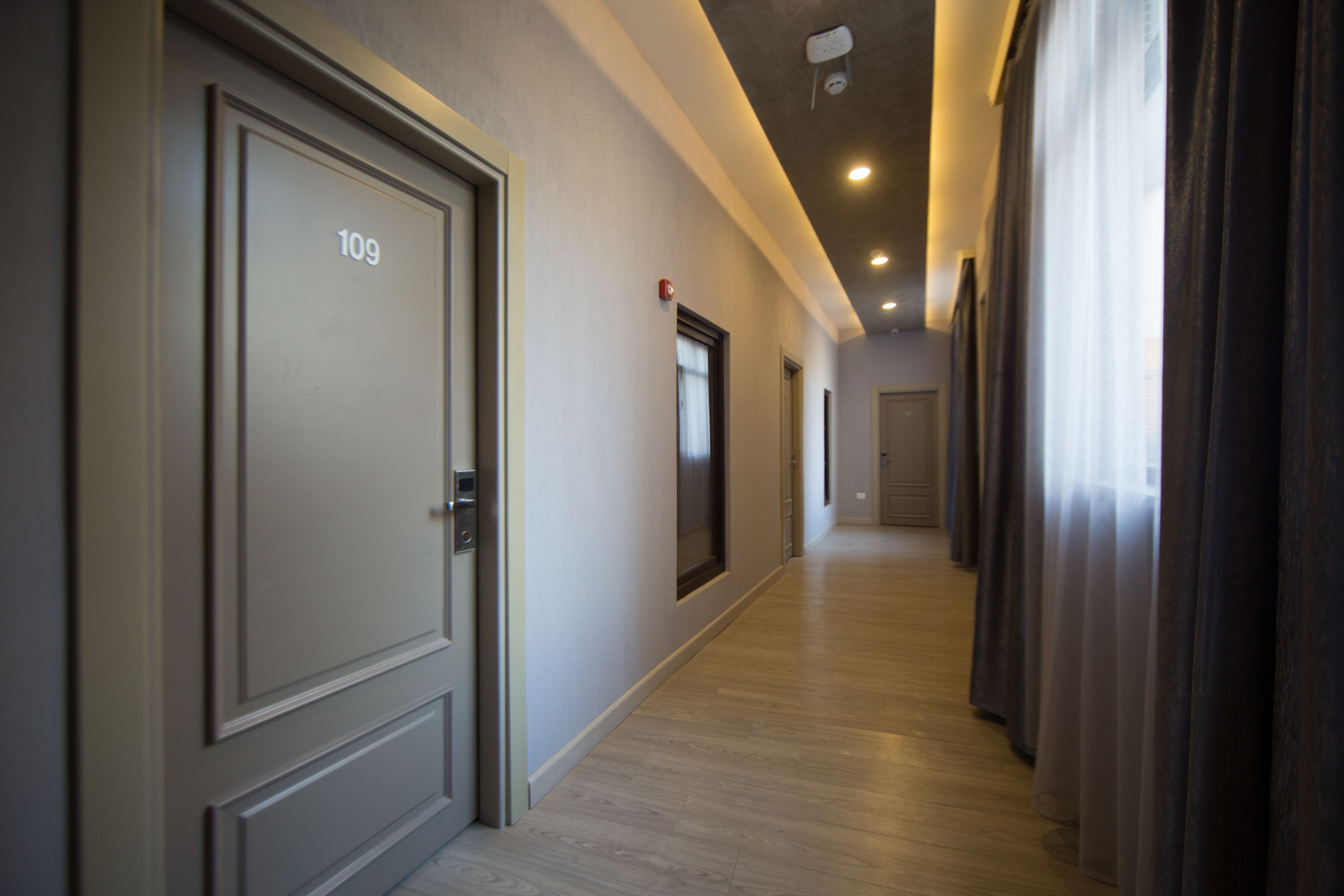 A hotel hallway with doors numbered 109 and 110, wooden flooring, and a ceiling with recessed lighting.