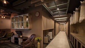 Corridoio d'hotel dalla forma lunga e stretta, con reception, area salotto e orologio a parete.