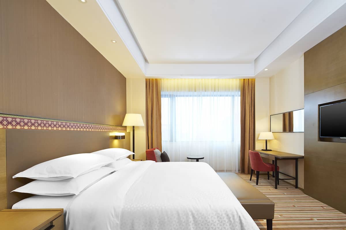 Una habitación de hotel con una cama grande, un escritorio, una silla, un televisor y una ventana con cortinas.