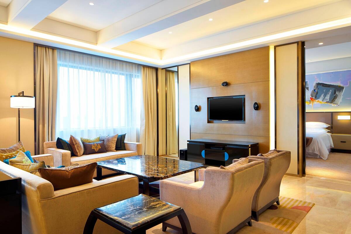 Una habitación de hotel moderna con sofá, sillones, una mesa de centro, televisor de pantalla plana y cama.
