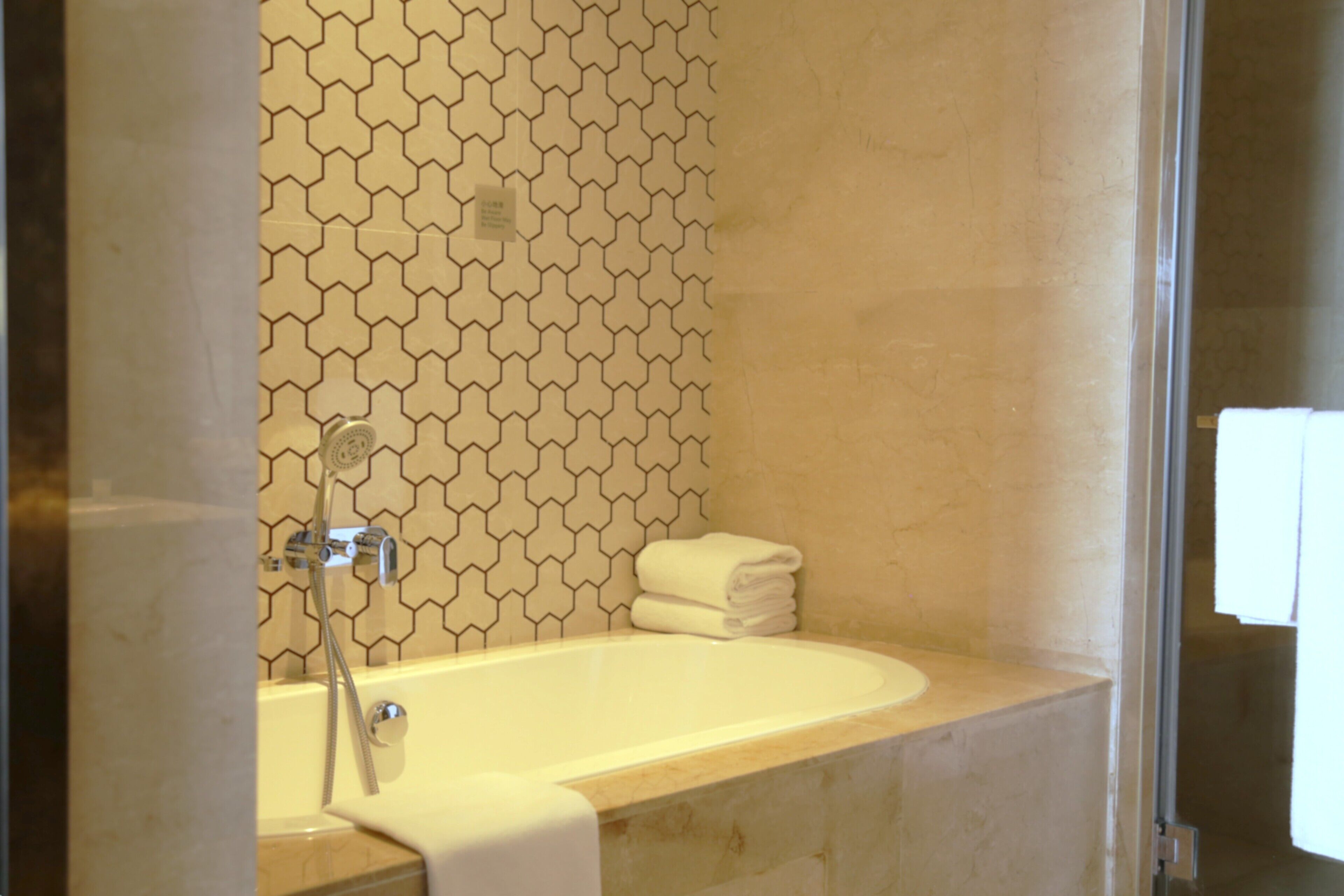 Een badkamer met een bad, een douche en een betegelde wand.