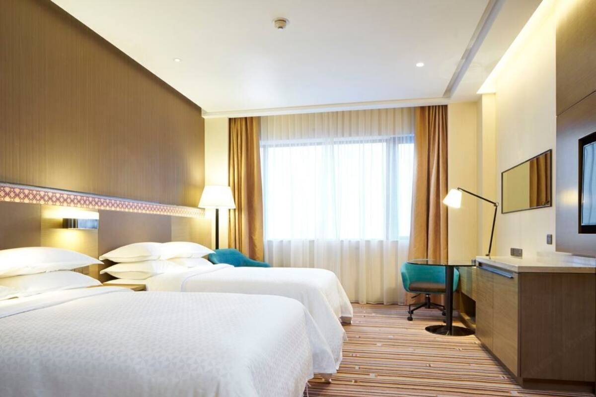 Habitación de hotel con dos camas, un escritorio, una silla y un ventanal con cortinas.