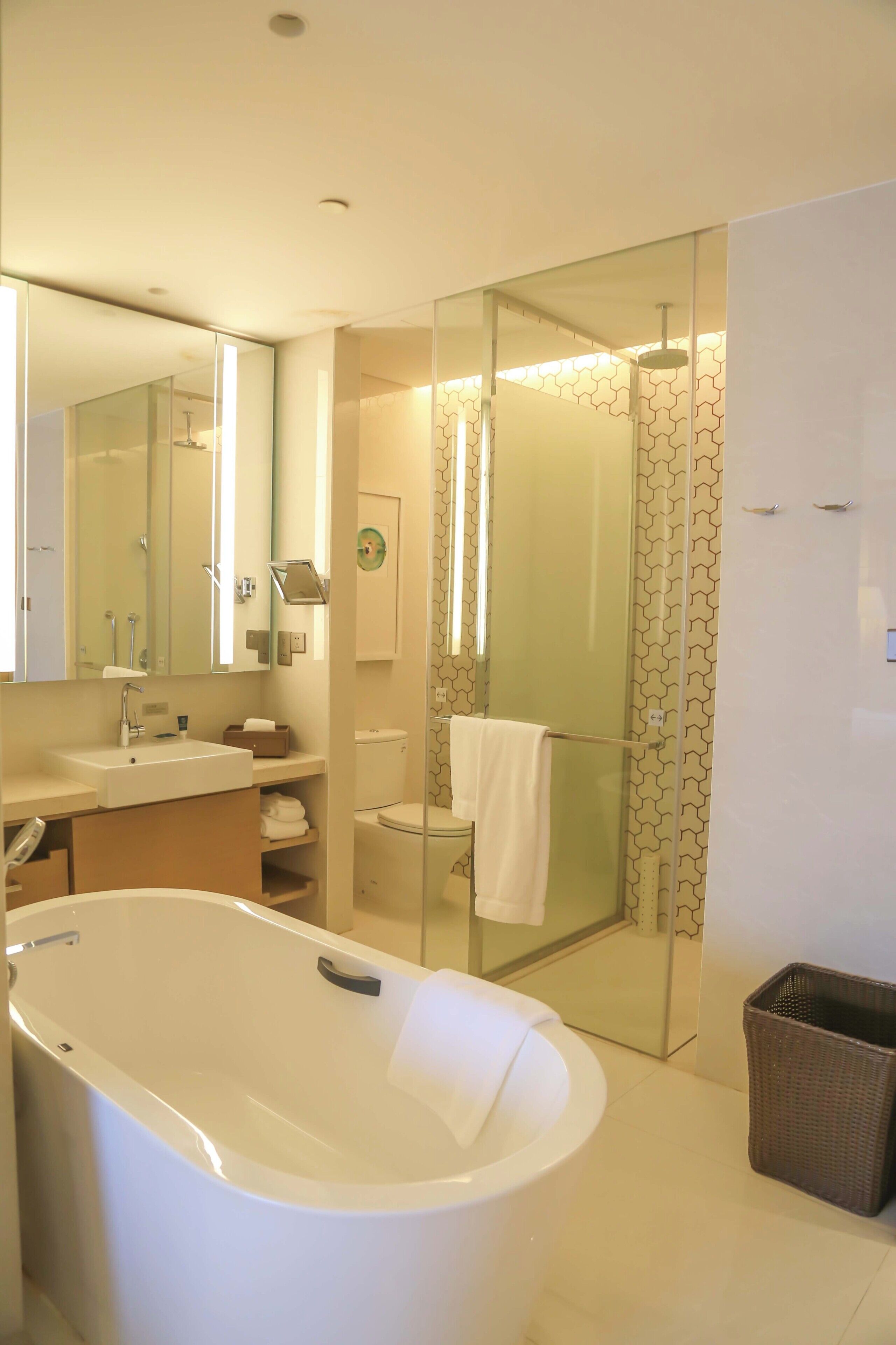 Un baño moderno con bañera, mampara de vidrio, lavamanos con espejo e inodoro.