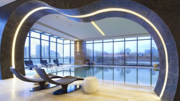 A modern indoor pool area with a large glass window, lounge chairs, and a unique architectural design. - Four Points By Sheraton Guilin, Lingui (Guilin)