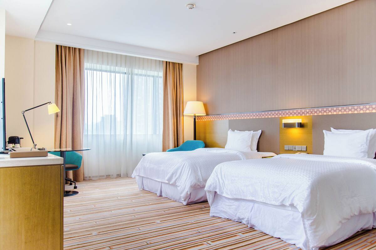 Una habitación de hotel con dos camas, un escritorio, una silla y una lámpara.