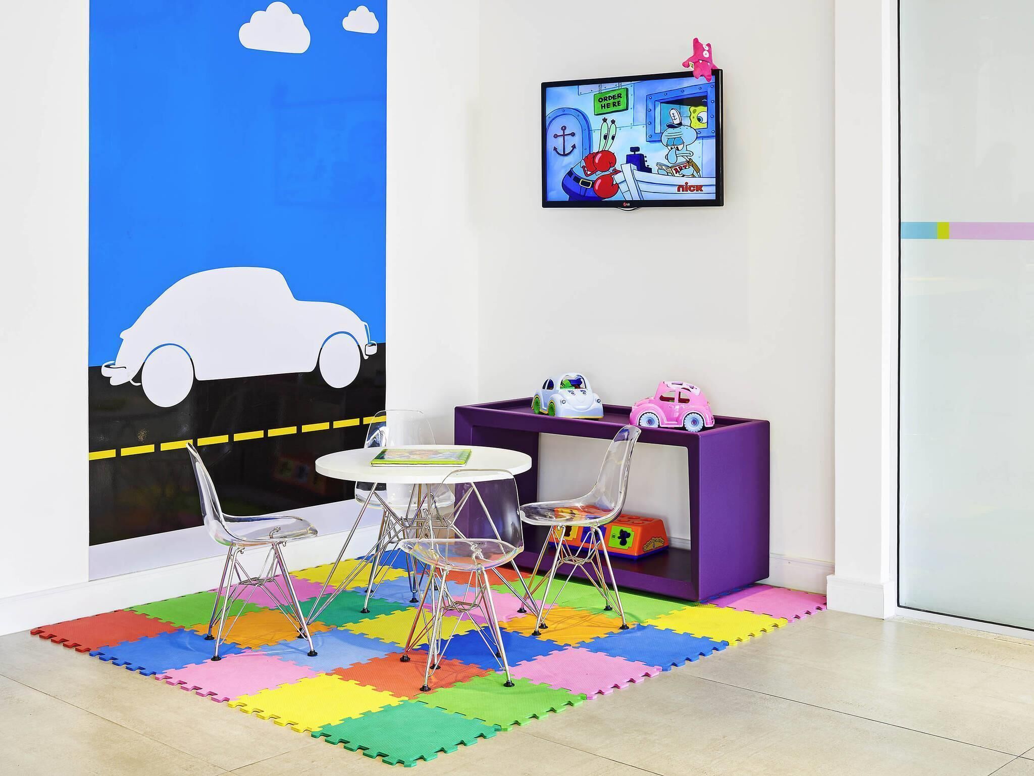 Uma área de recreação infantil com adesivo de parede de carros, uma televisão e um móvel de armazenamento roxo.