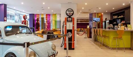 A vintage car exhibit in a modern indoor setting with a bar area and seating.