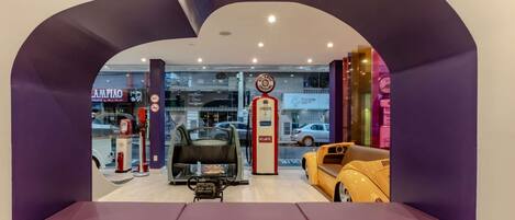 Un área de espera con un banco, exhibición de automóviles y bomba de gasolina.