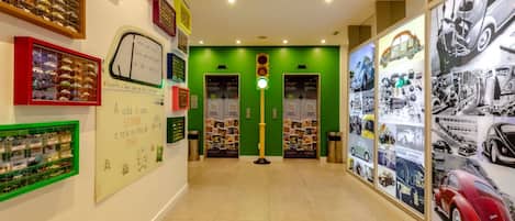 Un couloir aux murs verts, doté d’un sol carrelé et agrémenté de diverses présentations et affiches sur le thème de l’automobile.