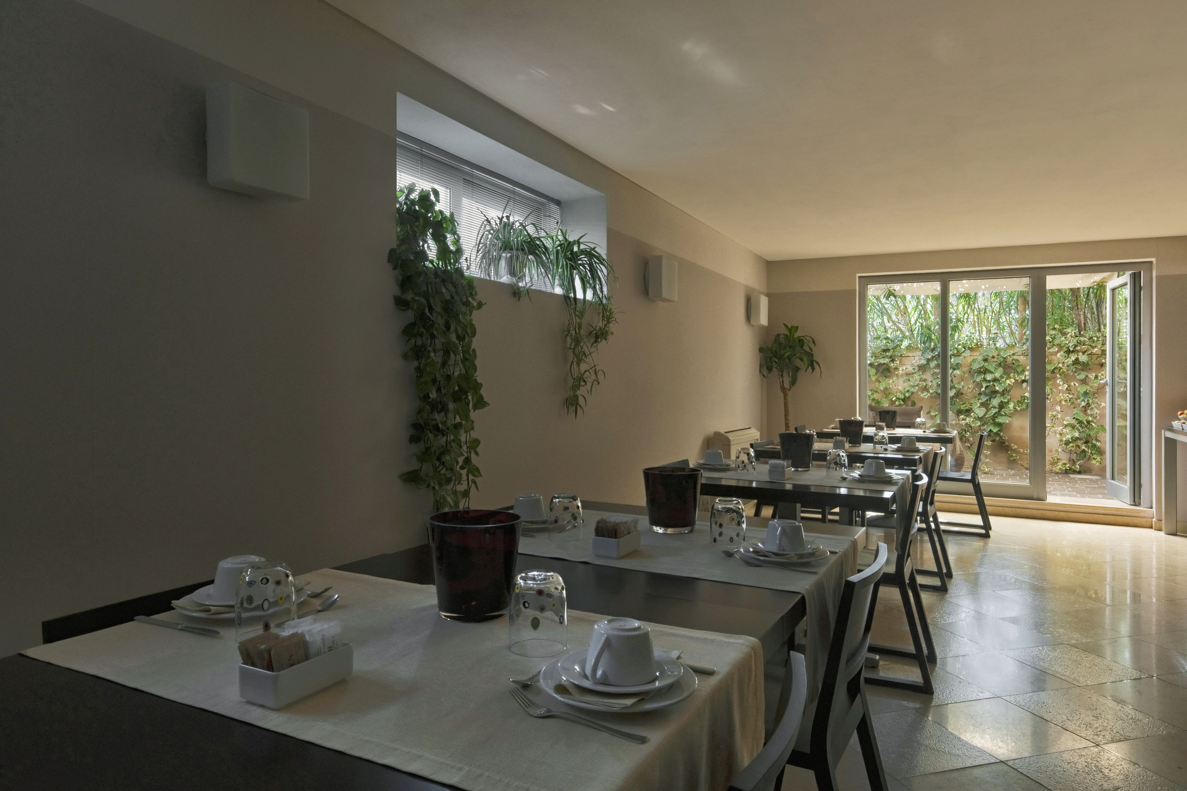 Comedor con mesas dispuestas para una comida, plantas en macetas y vistas al exterior.