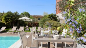 A poolside area with lounge chairs, a table with a white umbrella, and a potted plant with blue flowers. - Vialeromadodici Rooms & Apartments (Lazise)