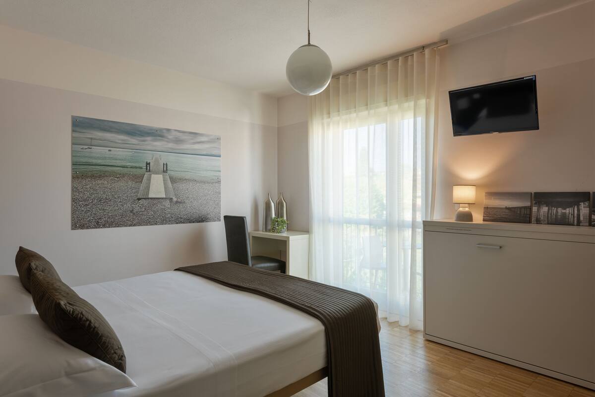 A bedroom with a bed, a desk, a TV, and a painting on the wall.