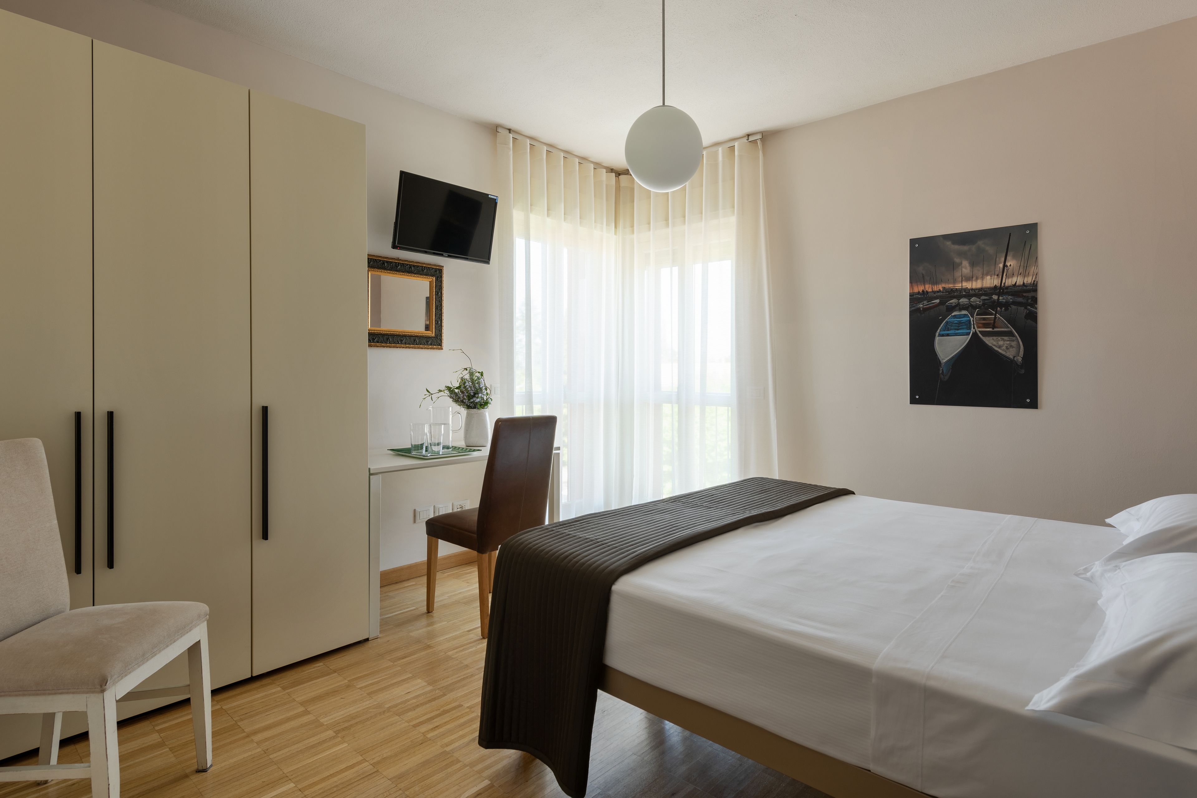 Habitación de hotel con una cama, un escritorio con silla, un televisor y un cuadro en la pared.