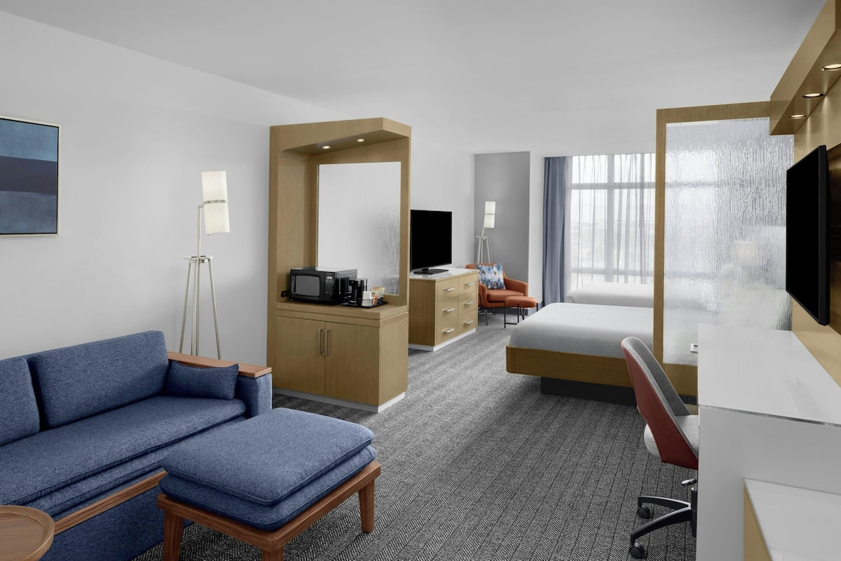 Habitación de hotel con sofá, escritorio, televisión, cama, cómoda y ventana con vista.