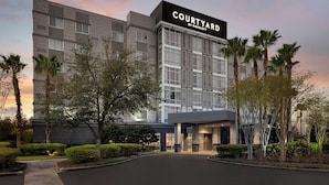 Un hotel moderno con un llamativo letrero de 'Courtyard by Marriott', que presenta un diseño limpio y contemporáneo con un amplio frente de vidrio y un área de entrada ajardinada y bien cuidada.