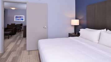 Habitación de hotel con una cama grande, una lámpara de noche, un escritorio con silla y vista a un pasillo con un cuadro.