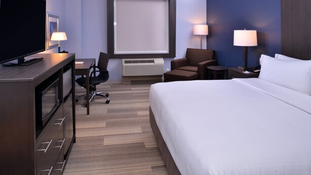 Een hotelkamer met een bed, een bureau met een televisie, twee stoelen, een lamp en een raam.