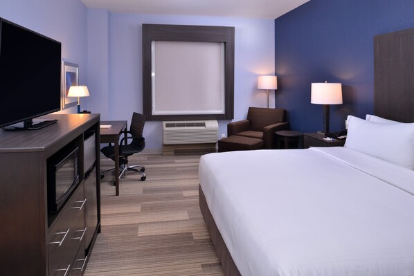 Habitación de hotel con cama, escritorio con televisor, dos sillas, lámpara y ventana.