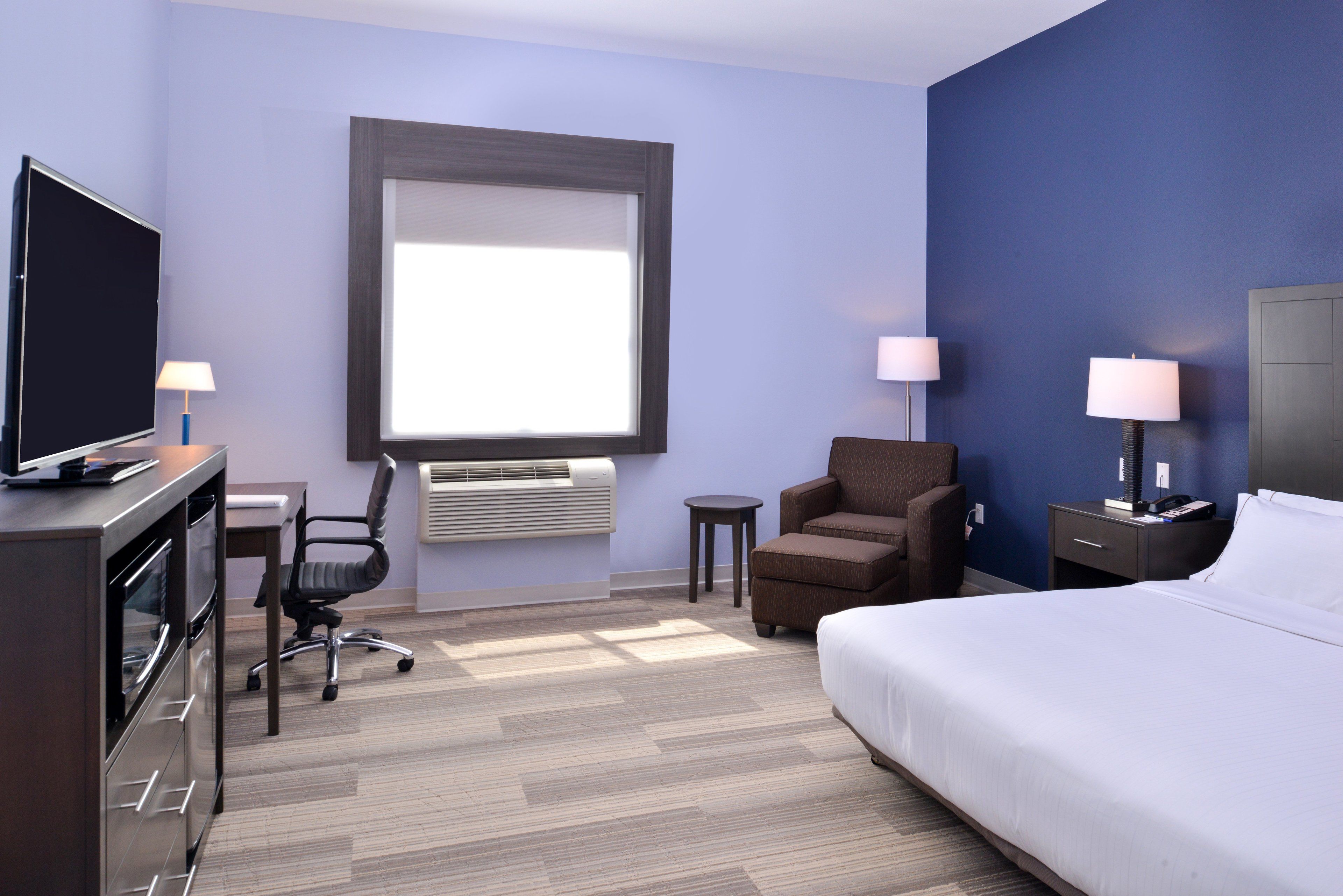 Habitación de hotel con una cama, un escritorio con computadora, una silla, una mesita y un televisor.