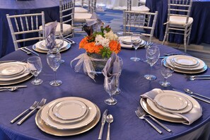 Mesa redonda dispuesta para un evento formal, con varios puestos individuales que incluyen platos, vasos y cubiertos.