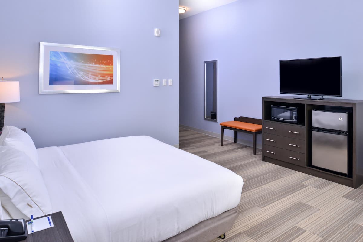 A hotel room with a large bed, a TV, a microwave, and a bench.