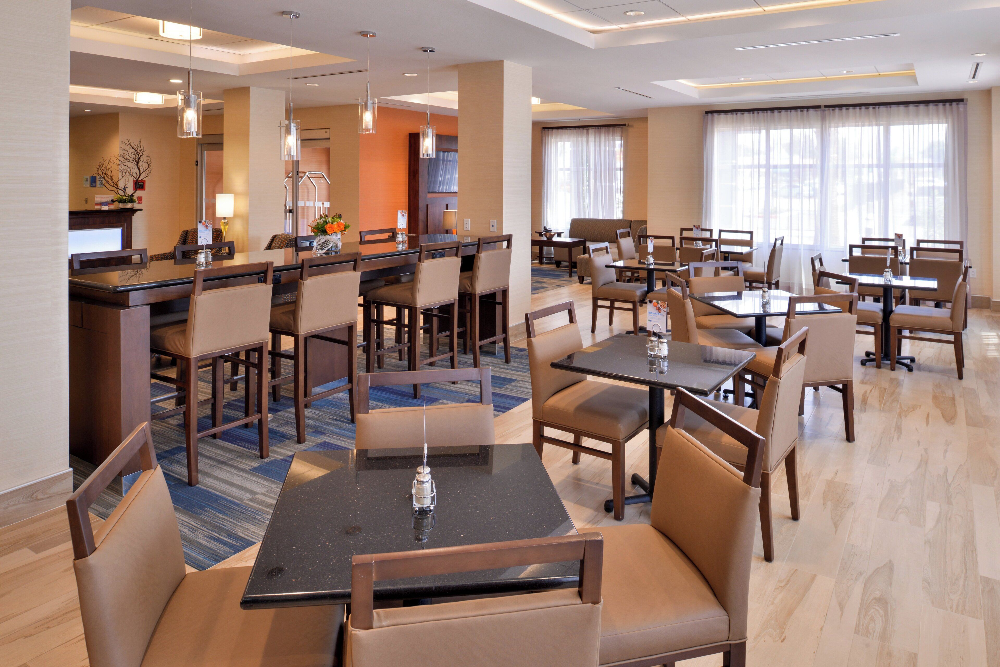 Un comedor de hotel con varias mesas y sillas, una recepción y un ventanal con cortinas.