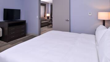 Ein Hotelzimmer mit einem Bett, einem Fernseher auf einer Kommode, einer Lampe und einer Tür zu einem Sitzbereich.