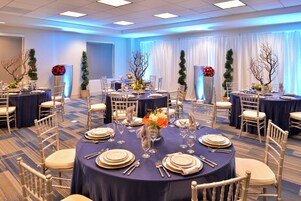 Un salón de conferencias de hotel con mesas redondas, sillas y centros de mesa con flores.