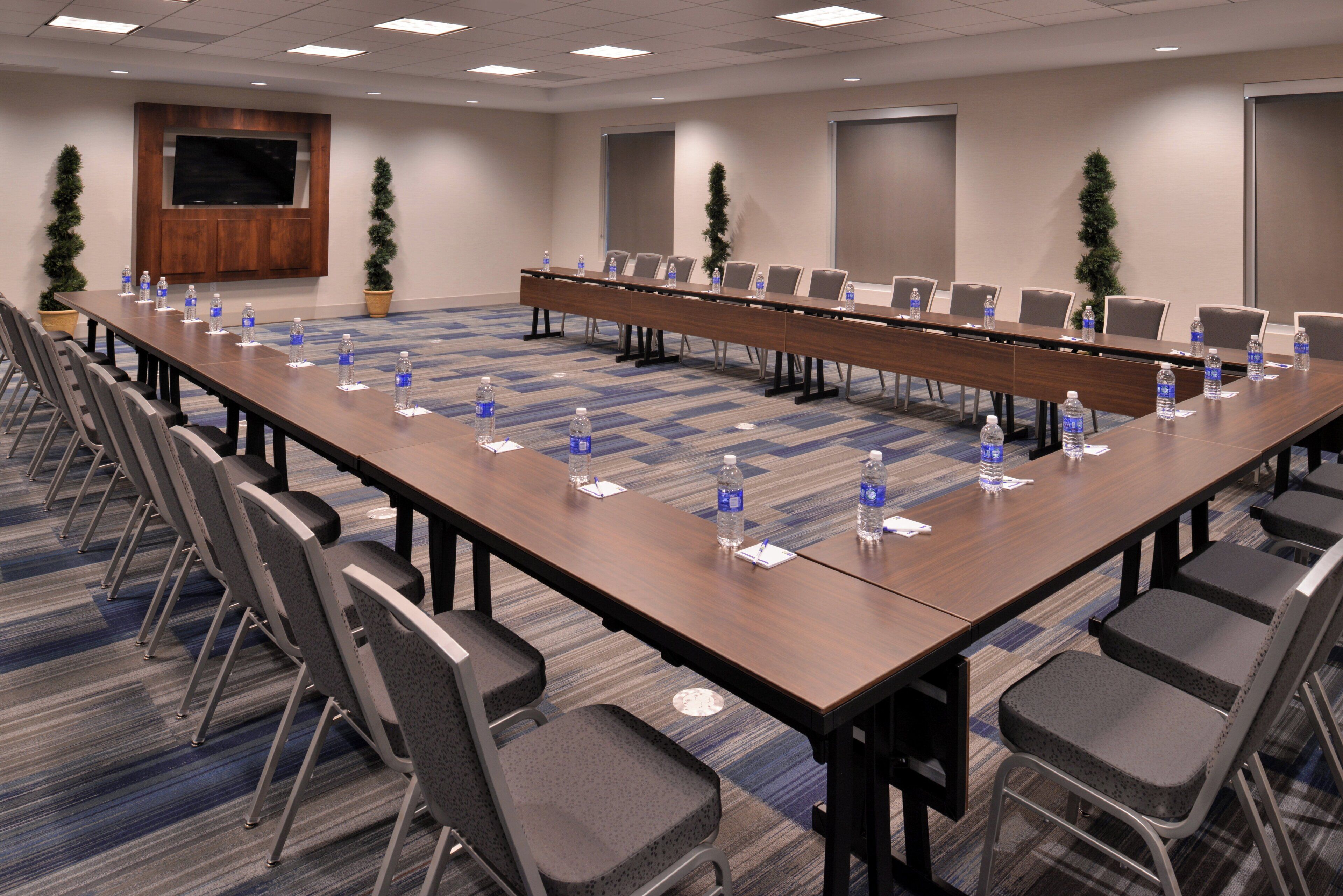 Une salle de conférence avec une longue table, des chaises, des bouteilles d’eau et un téléviseur fixé au mur.