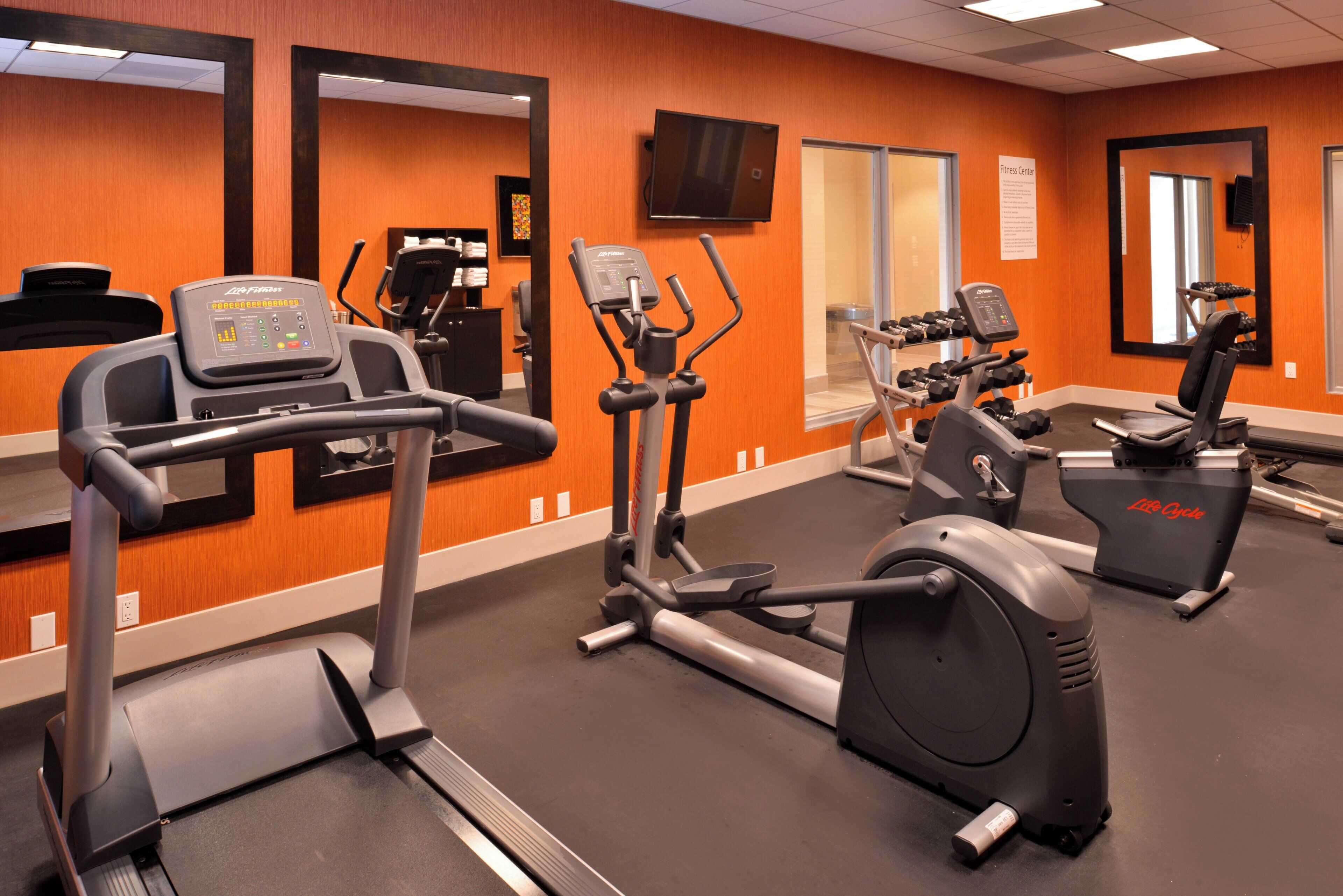 A gym with cardio machines, mirrors, and a TV.