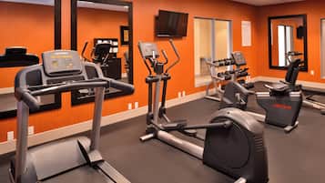 A gym with cardio machines, mirrors, and a TV.