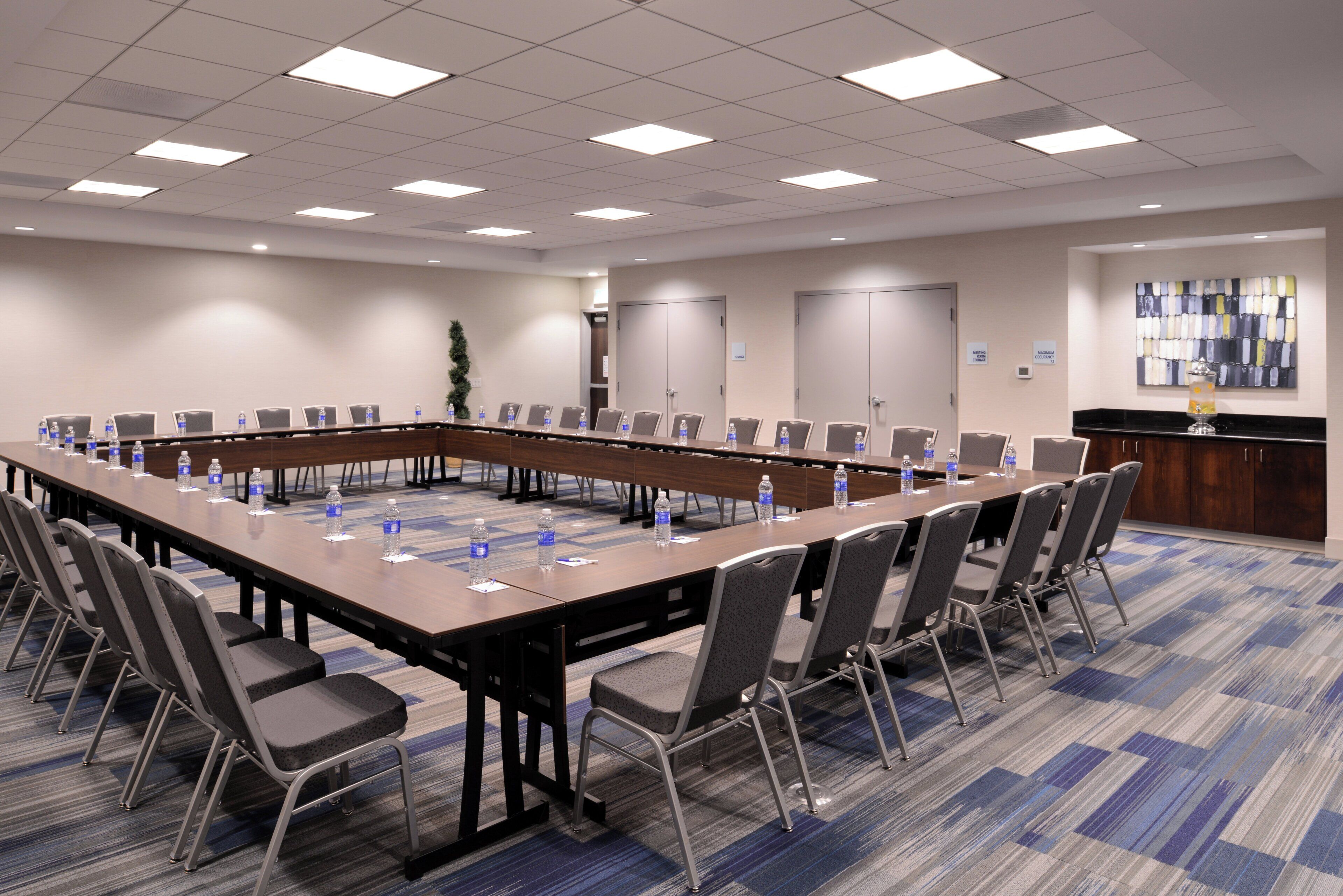 Una sala de conferencias con una larga mesa, sillas, botellas de agua y una estación de café.
