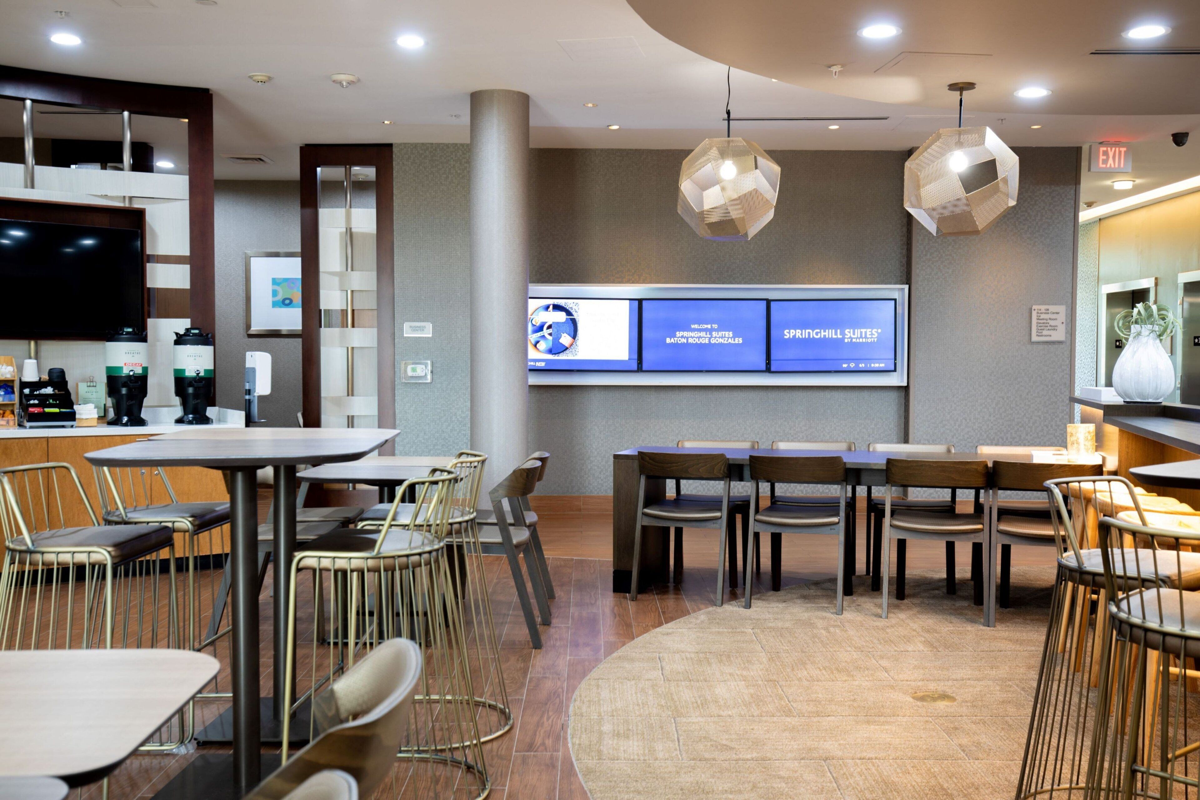 A modern hotel lobby with a reception desk, seating area, and digital screens displaying room information.