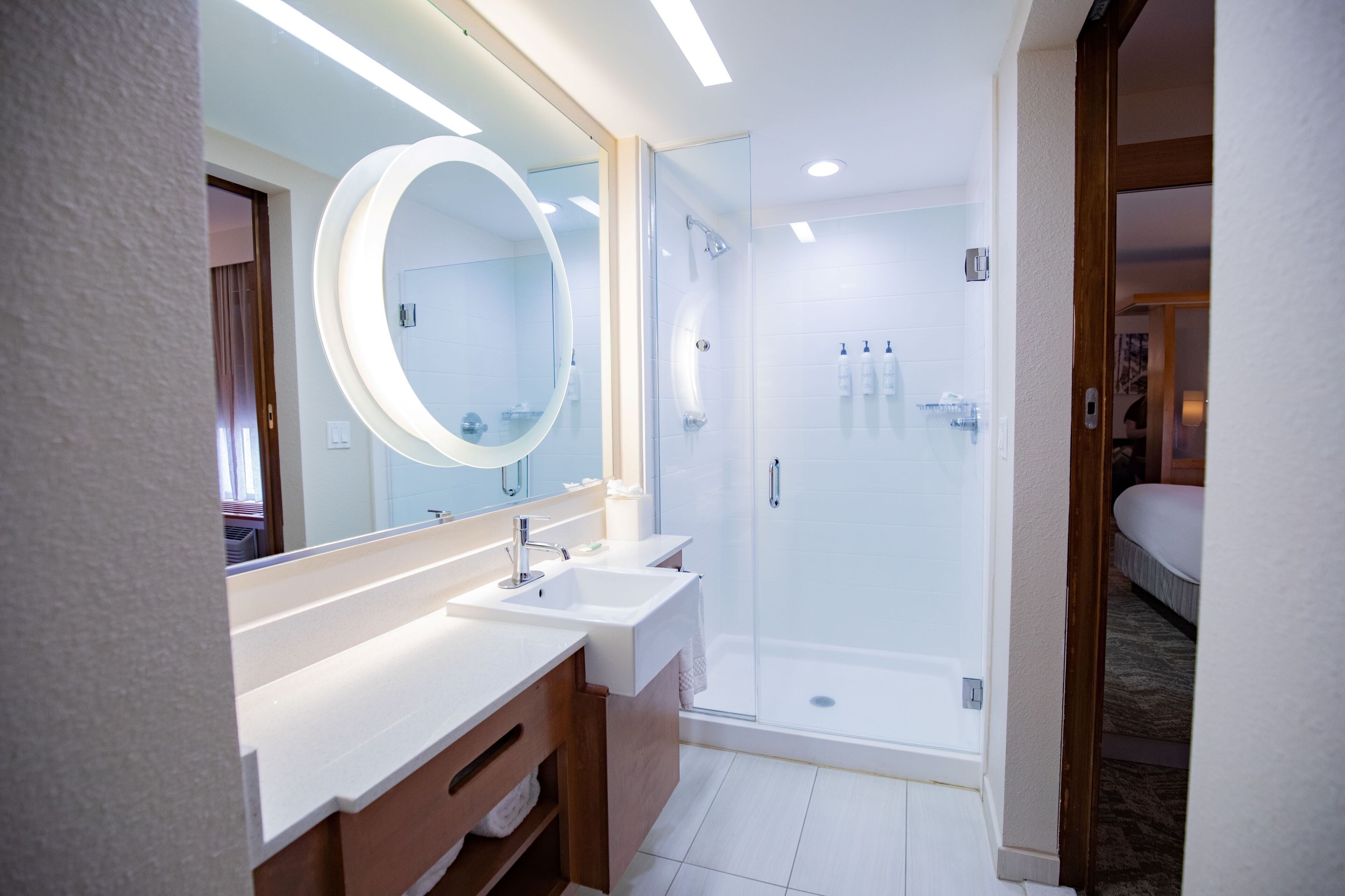 A modern bathroom with a large mirror, two sinks, a shower, and a toilet.