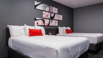 Een hotelkamer met twee bedden, elk voorzien van witte beddengoed en rode sierkussens, en een modern kunstwerk erboven.